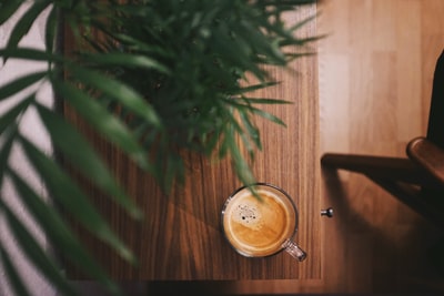 棕色桌子上植物旁的透明玻璃杯中盛满半杯咖啡